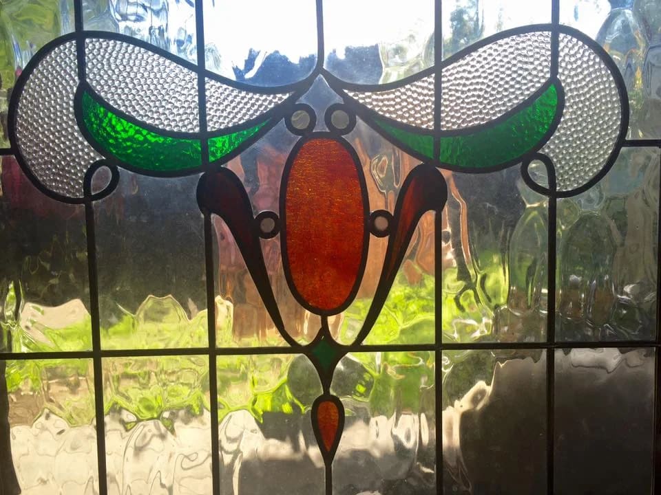 Stylised amber tulip and whiplash stems in leadlight, garden greenery behind