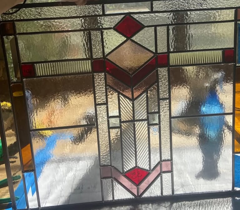 Art Deco panel with a stepped fountain motif in red, amber and reeded clear glass, backlit on the studio bench