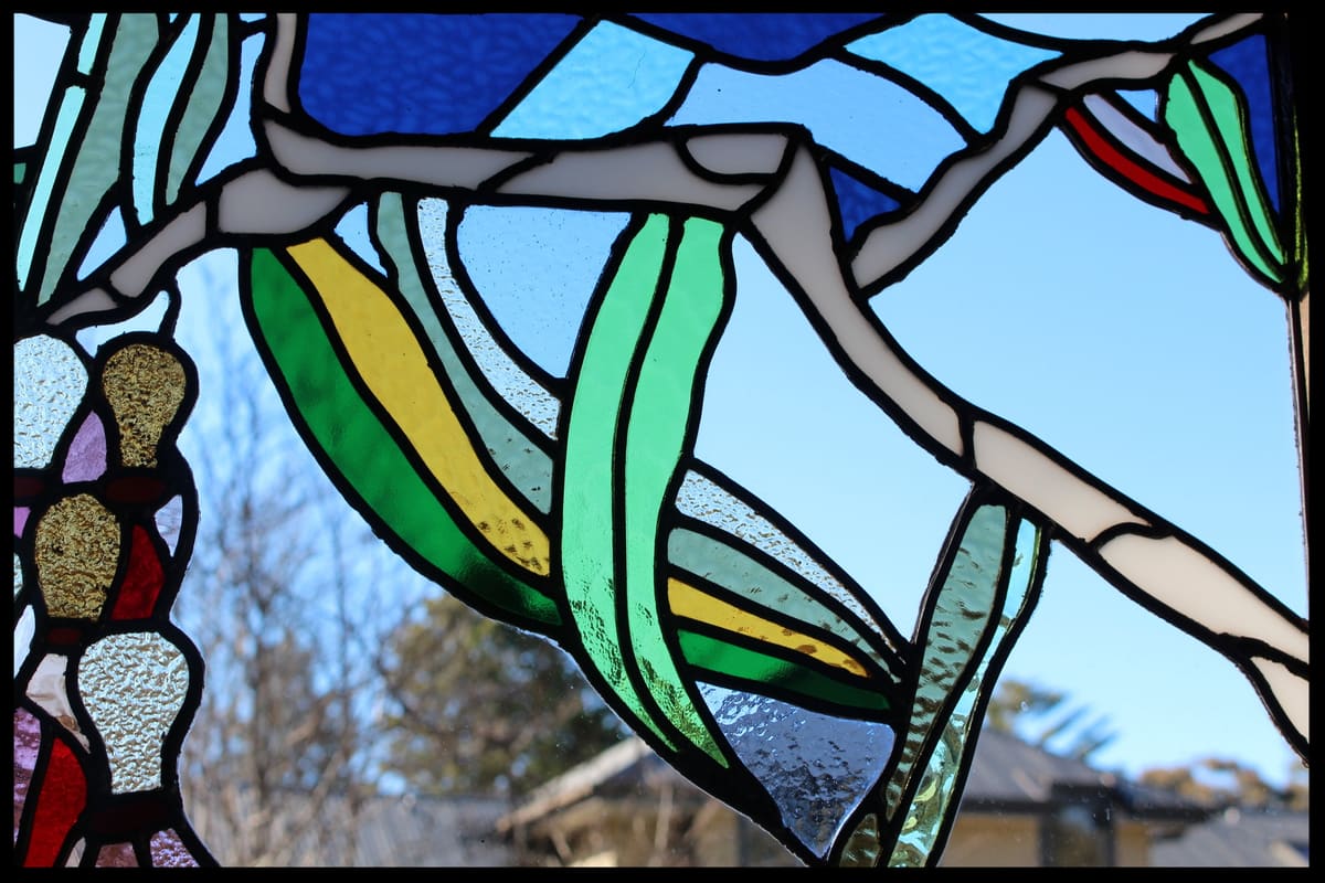 Angophora leadlight close-up in bold green and gold glass, a garden and house behind