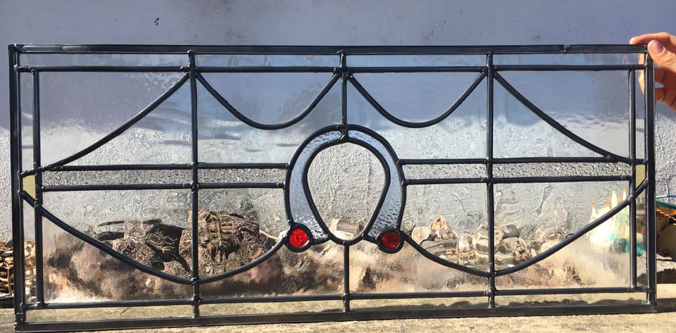 Art Deco horseshoe fanlight in leadlight with ruby jewels, backlit against a stone wall