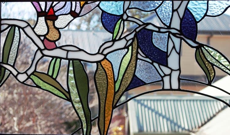 Companion wattle and gum-leaf panel in leadlight, backlit against a bright blue sky
