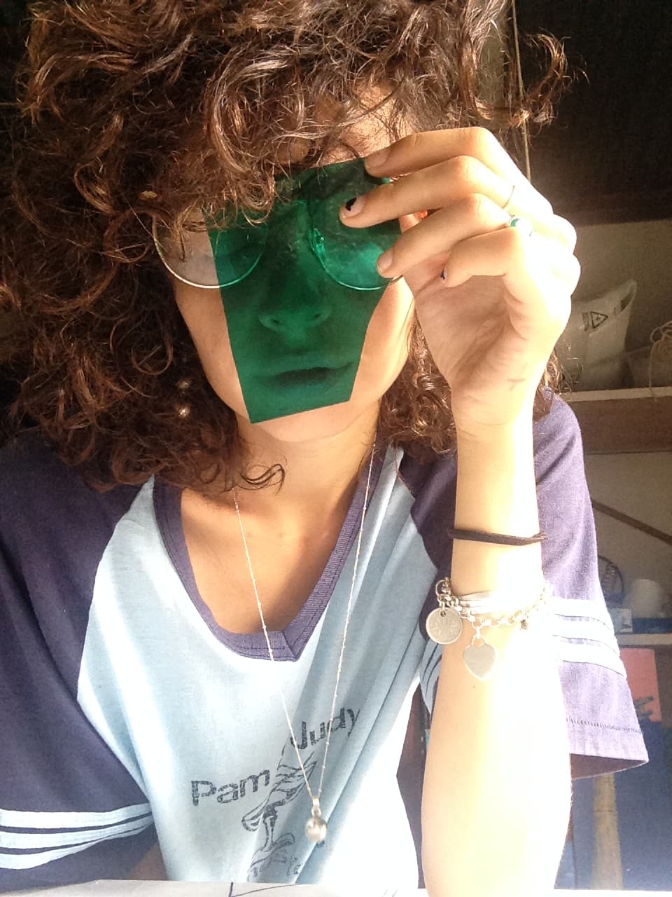 Kirby holding a piece of coloured glass up to her face in the studio