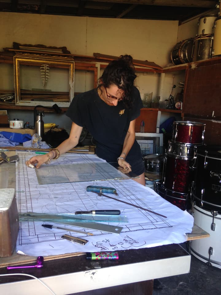 Kirby working at the cutting table surrounded by tools and plans