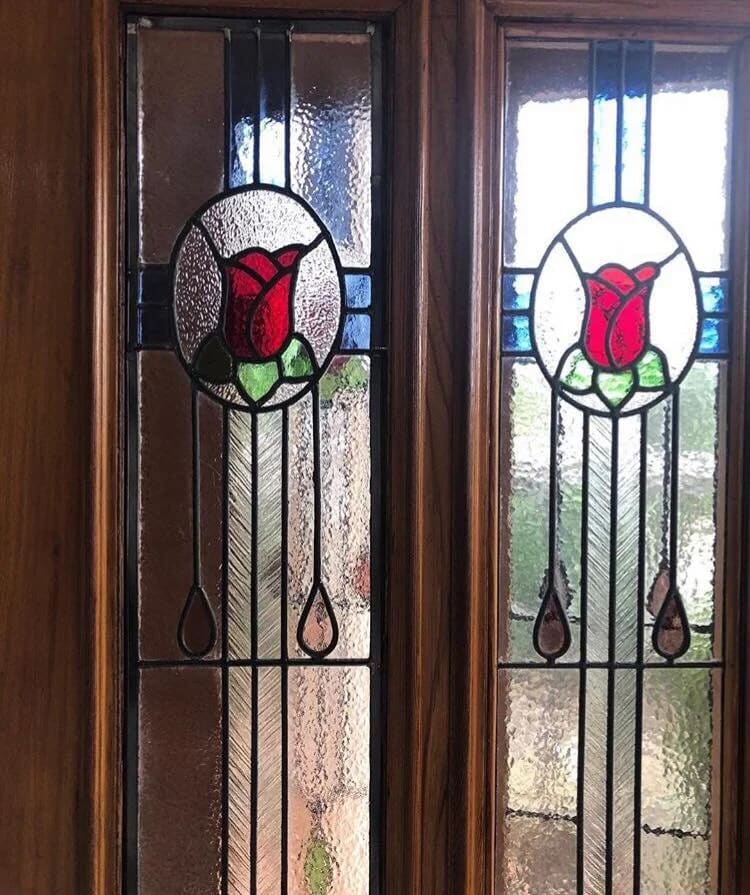 Pair of Federation sidelights in a timber door, each an oval-framed red rose on a whiplash stem